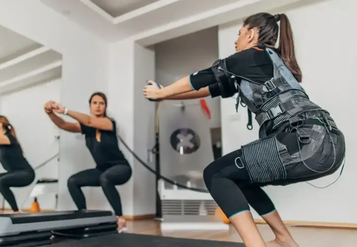 Kobiety w kamizelkach EMS wykonują przysiady. Trening z elektrostymulacją mięśni (EMS) to przyszłość fitnessu.
