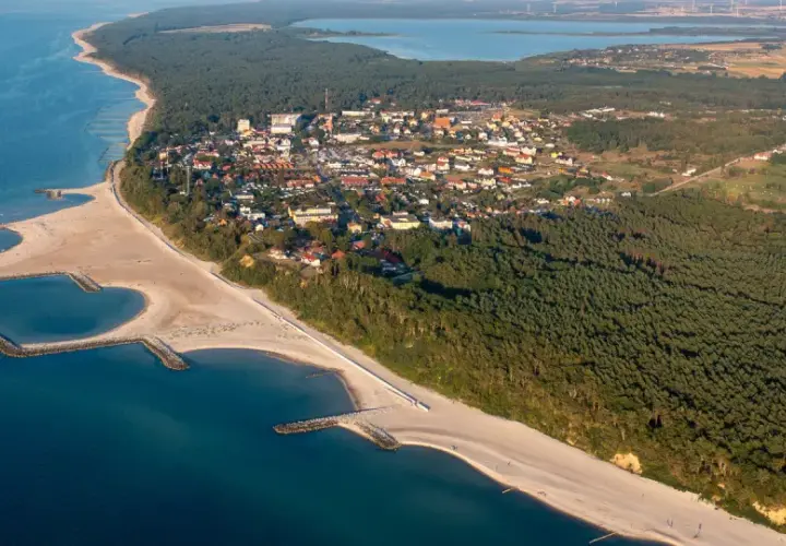 Widok z lotu ptaka na Jarosławiec, nadmorską miejscowość z piaszczystą plażą, lasami i zabudowaniami.