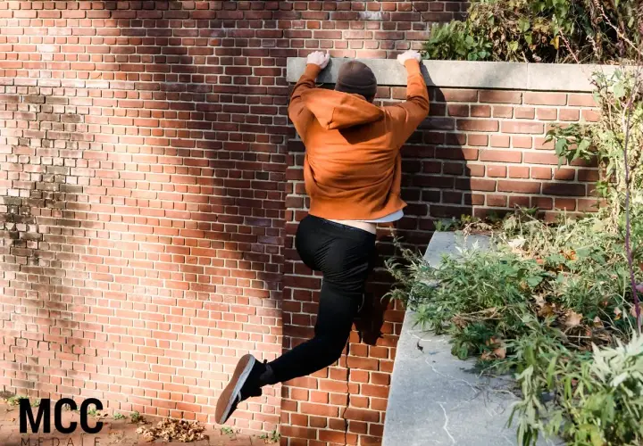Młody człowiek wspina się po ceglanej ścianie, pokazując, czym jest parkour.