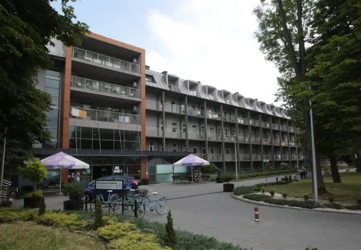 Budynek sanatorium z balkonami i drzewami. Miejsce idealne do wypoczynku i regeneracji, gdzie balneologia odgrywa kluczową rolę.