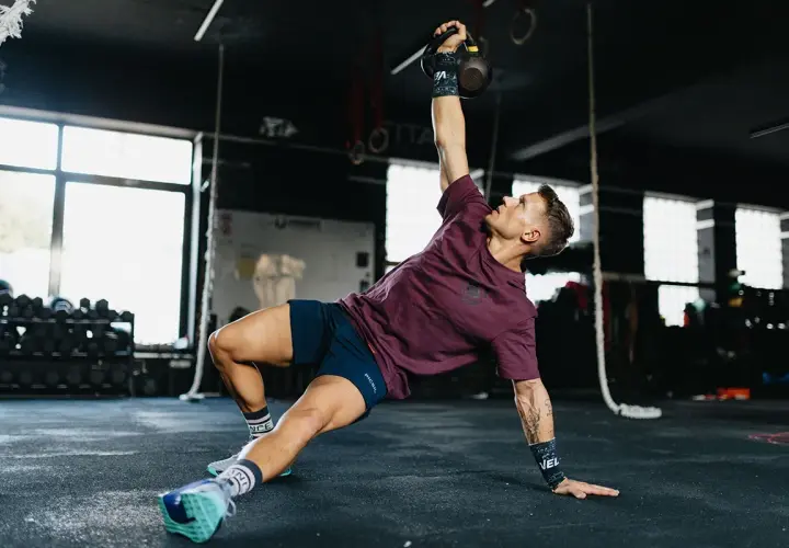 Mężczyzna wykonuje ćwiczenia gimnastyczne z kettlebell, unosząc go nad głowę.