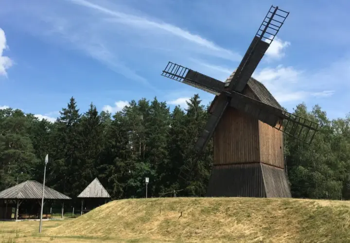 Drewniany wiatrak na wzgórzu, otoczony lasem, w tle błękitne niebo z chmurami. Miejsce jak z bajki w Obornikach Śląskich.