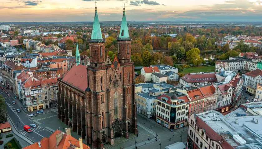Widok z lotu ptaka na miasto nad Kaczawą. Dominują ceglana katedra z zielonymi wieżami i kolorowe kamienice.