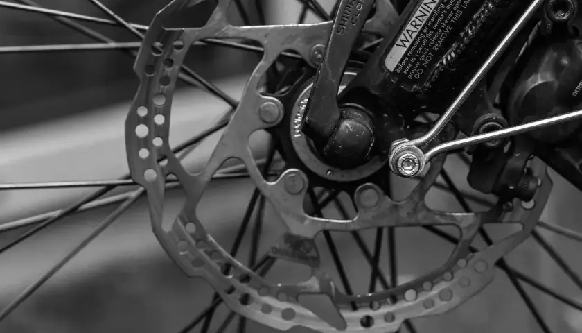 Tarcza hamulcowa i szprychy roweru. Widoczny mechanizm przerzutek Shimano i ostrzeżenie.