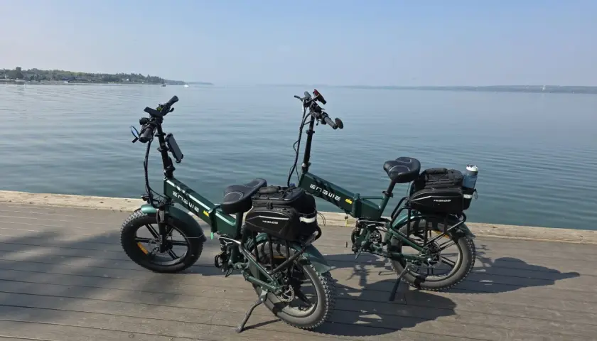 Dwa zielone rowery elektryczne z sakwami, gotowe na wyprawę z zasięgiem 200 km nad spokojną wodą.