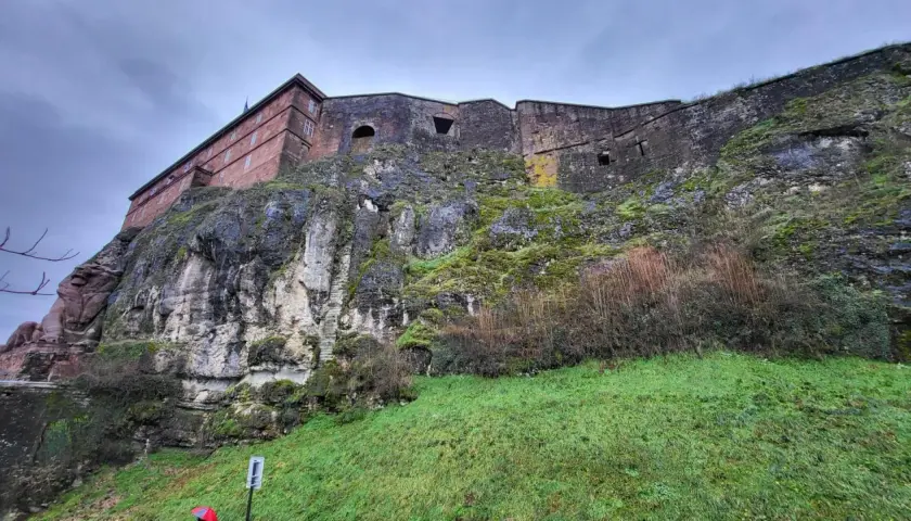 Potężny belfort wznosi się na skalistym zboczu porośniętym mchem. Kamienne mury i zielona trawa tworzą imponujący widok.