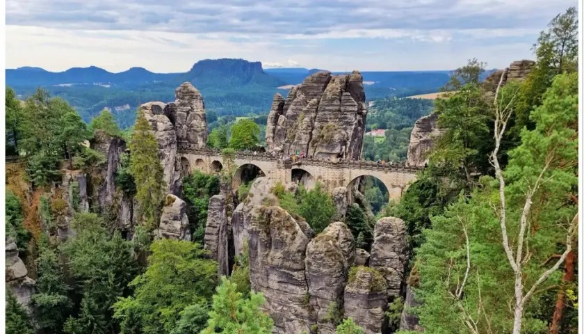 Kamienny most Bastei w Saksońskiej Szwajcarii, łączący skalne baszty pośród zielonych lasów i gór.