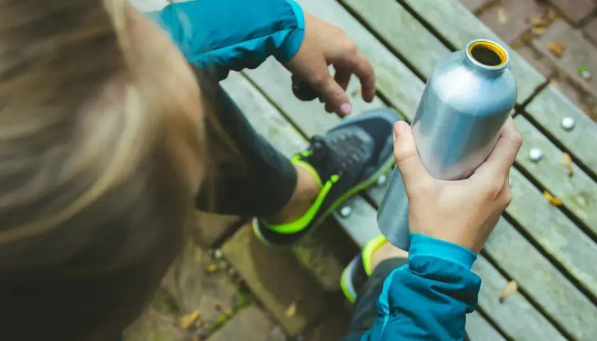 Osoba w sportowej kurtce i butach z neonowymi wstawkami trzyma metalową butelkę. W środku pewnie jest izotonik, idealny po wysiłku.