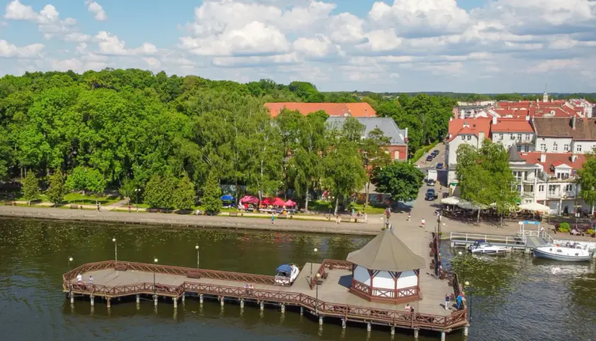 Malownicze mazury miejscowości nad jeziorem, z drewnianym molo, altaną i urokliwą zabudową.