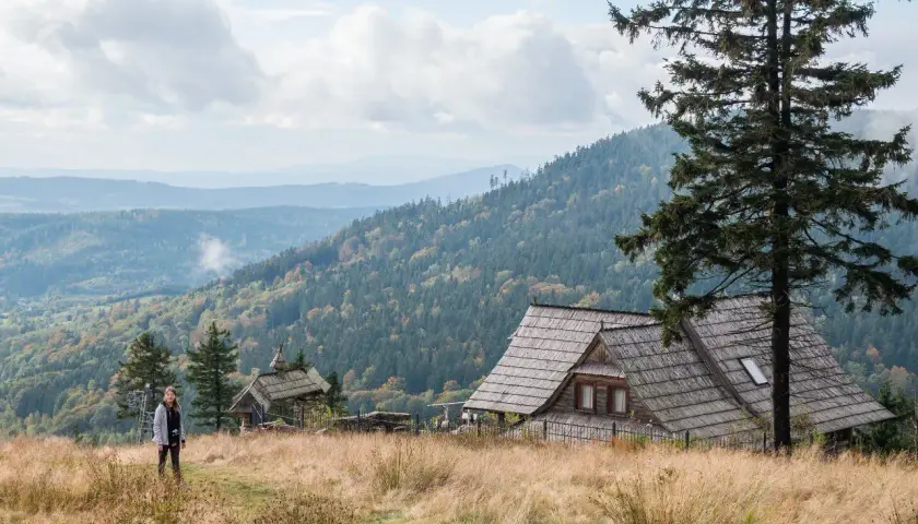Dziewczyna na tle malowniczych gór Dolnego Śląska. Drewniane chaty i lasy tworzą sielski krajobraz.