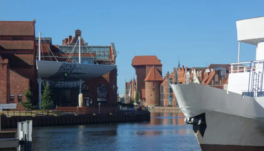 Widok na Motławę i zabytkowe kamienice gdańskiej starówki. Biały dziób statku na pierwszym planie.