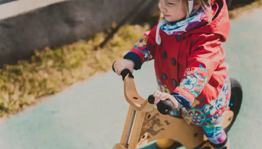 Mała dziewczynka w czerwonej kurtce na rowerku biegowym. Od jakiego wieku można zacząć przygodę z takim pojazdem?