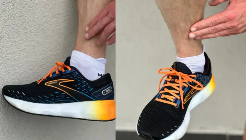 Biegacz pokazuje ból w łydce, który może być objawem shin splints. Na nogach ma czarne buty sportowe Brooks z pomarańczowymi sznurówkami.