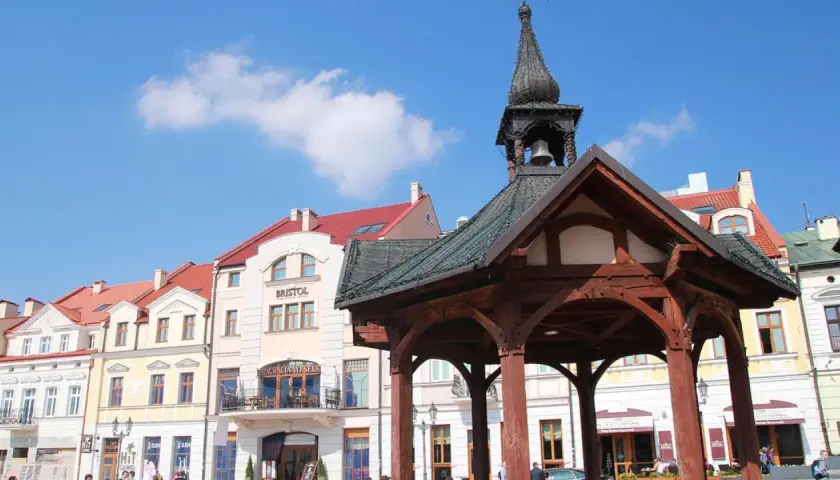 Rzeszów rynek z drewnianą altaną i kamienicami. Słońce świeci, a na niebie widać chmury.