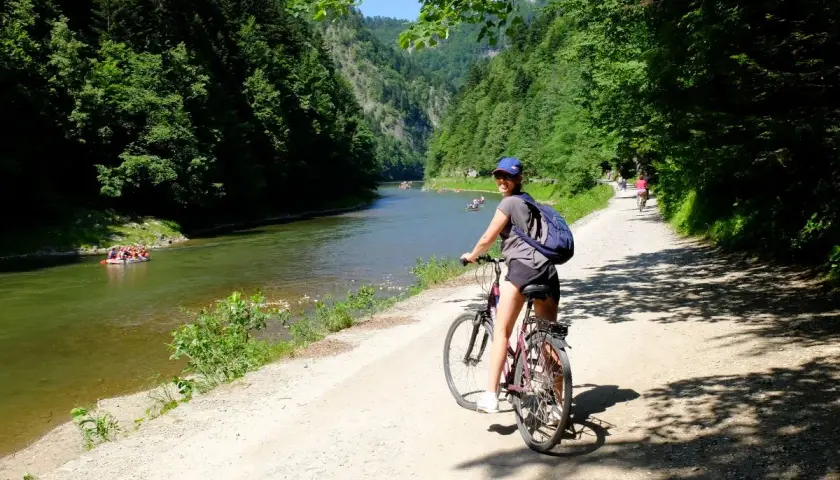 Dziewczyna na rowerze na malowniczej trasie rowerowej w Szczawnicy. W oddali widać tratwy na rzece.