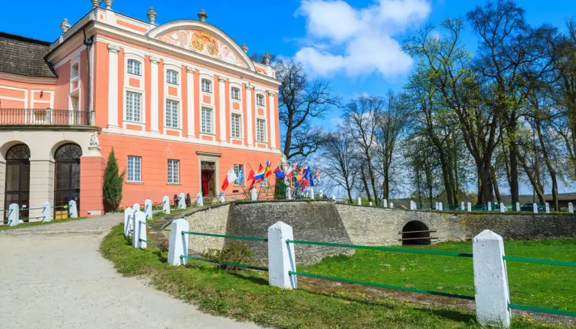 Pałac w Kurozwękach, z licznymi flagami przed wejściem, zaprasza do odkrywania jego atrakcji.