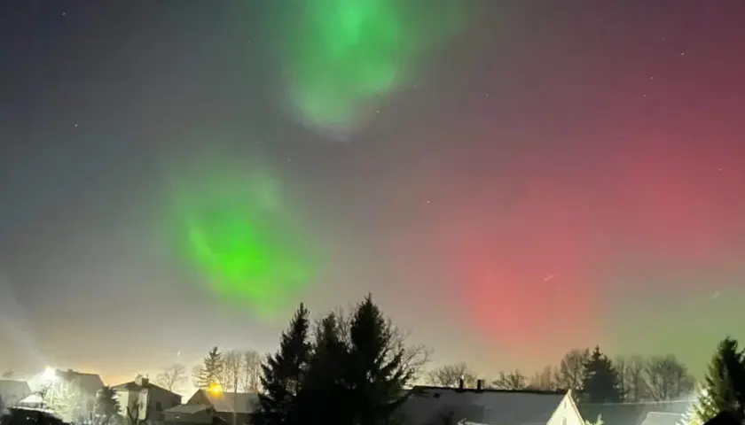 Zielona i czerwona zorza polarna nad domami. Zastanawiasz się, ile trwa zorza polarna? To zjawisko może trwać od kilku minut do kilku godzin.