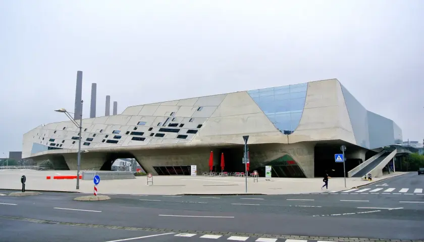 Futurystyczny budynek w Wolfsburg miasto, z betonowymi elementami i przeszklonymi fragmentami.
