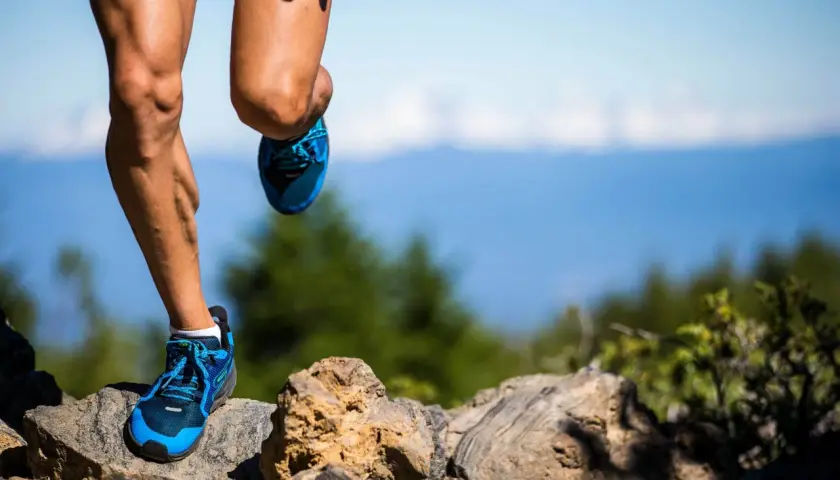 Nogi biegacza w niebieskich butach na kamienistym szlaku, przygotowującego się do ultramaratonu. Ile km jeszcze przed nim?