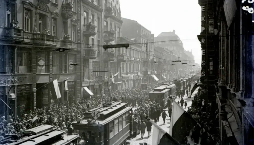 Tłum ludzi i tramwaje na ulicy Piotrkowska w Łodzi. Widać kamienice, flagi i napisy na sklepach.