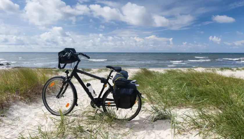 Rower z sakwami na piaszczystej plaży, gotowy na odkrywanie tras rowerowych nad morzem. Błękitne niebo i fale tworzą idealne tło.