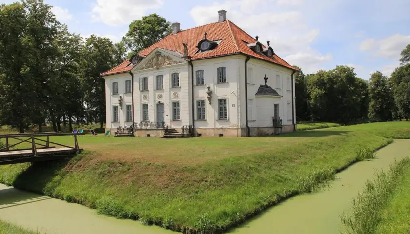 Pałac w Choroszczy otoczony fosą i zielenią. Drewniany mostek prowadzi do rezydencji.