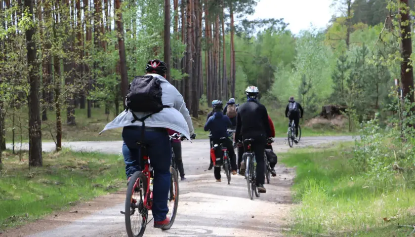 Grupa rowerzystów przemierza leśną ścieżkę. Każdy pedałujący spala kalorie, ciesząc się aktywnością na świeżym powietrzu.