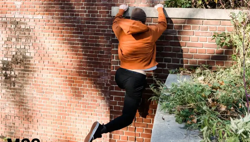 Młody człowiek wspina się po ceglanej ścianie, pokazując, czym jest parkour.