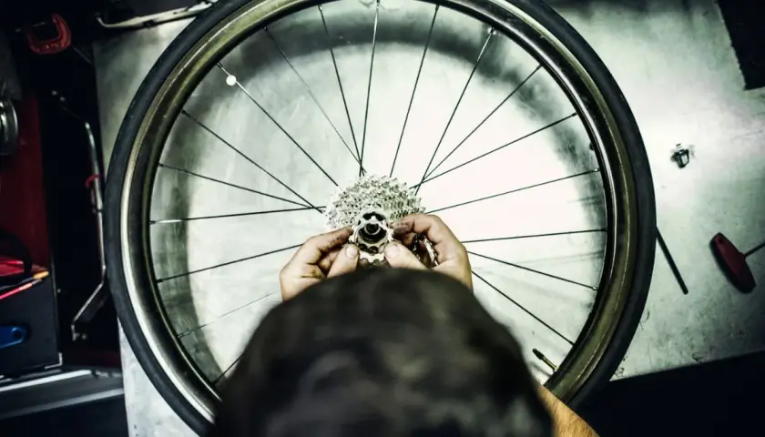 Ręce mechanika składają kasetę z zębatkami, przygotowując wolnobieg do montażu na kole rowerowym.