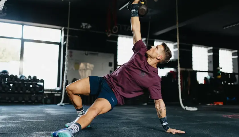Mężczyzna wykonuje ćwiczenia gimnastyczne z kettlebell, unosząc go nad głowę.