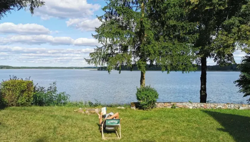 Osoba czyta książkę na leżaku nad jeziorem. To jedno z magicznych miejsc Kujawsko-Pomorskiego.