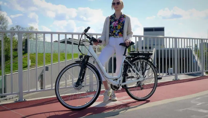 Kobieta z rowerem elektrycznym na moście. Czy na rower elektryczny trzeba mieć prawo jazdy? Zależy od jego mocy.