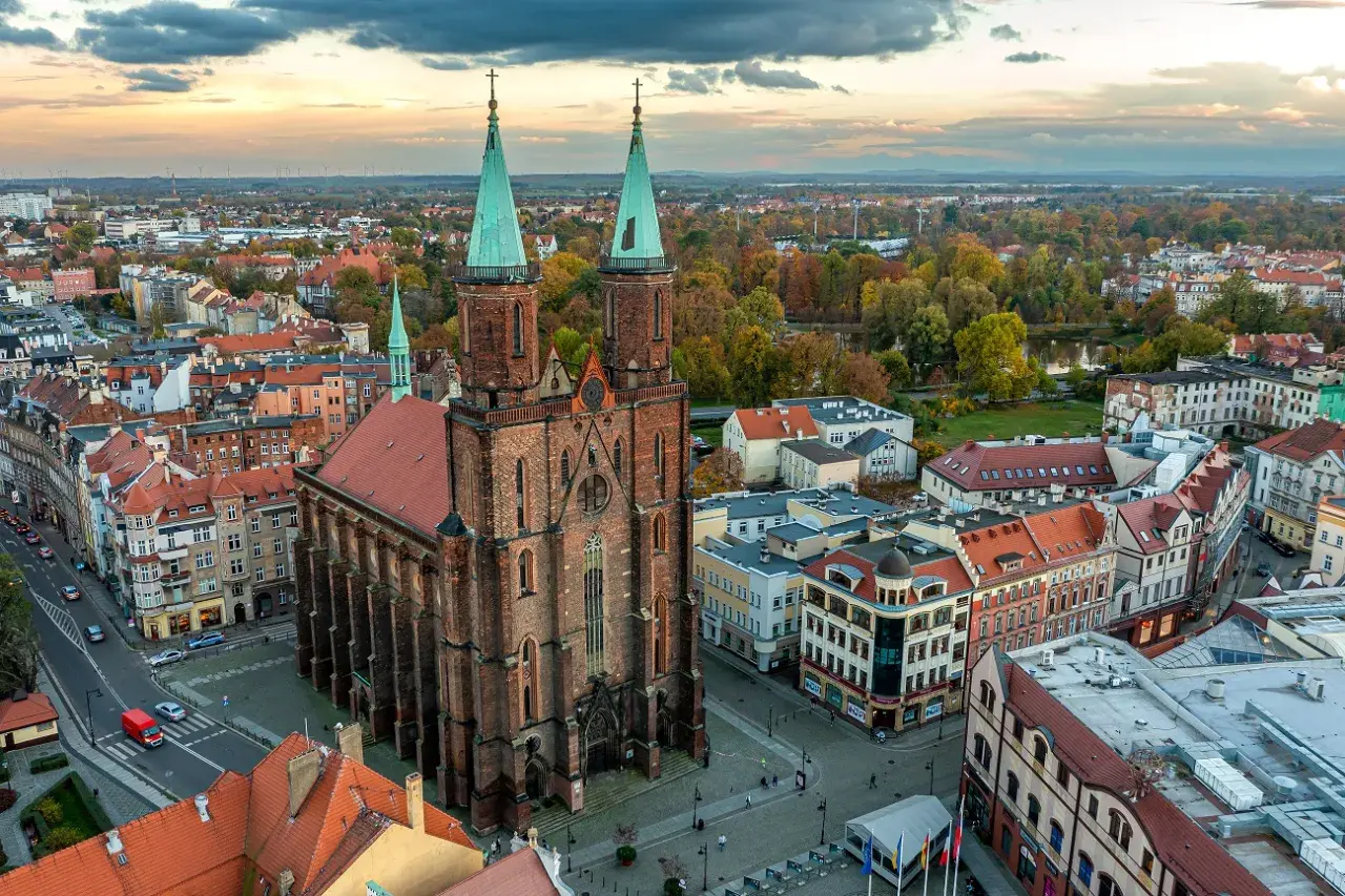 Widok z lotu ptaka na miasto nad Kaczawą. Dominują ceglana katedra z zielonymi wieżami i kolorowe kamienice.