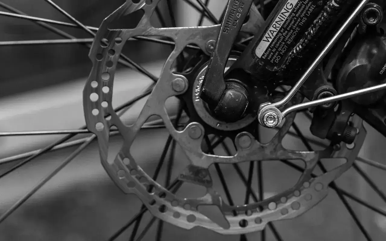Tarcza hamulcowa i szprychy roweru. Widoczny mechanizm przerzutek Shimano i ostrzeżenie.