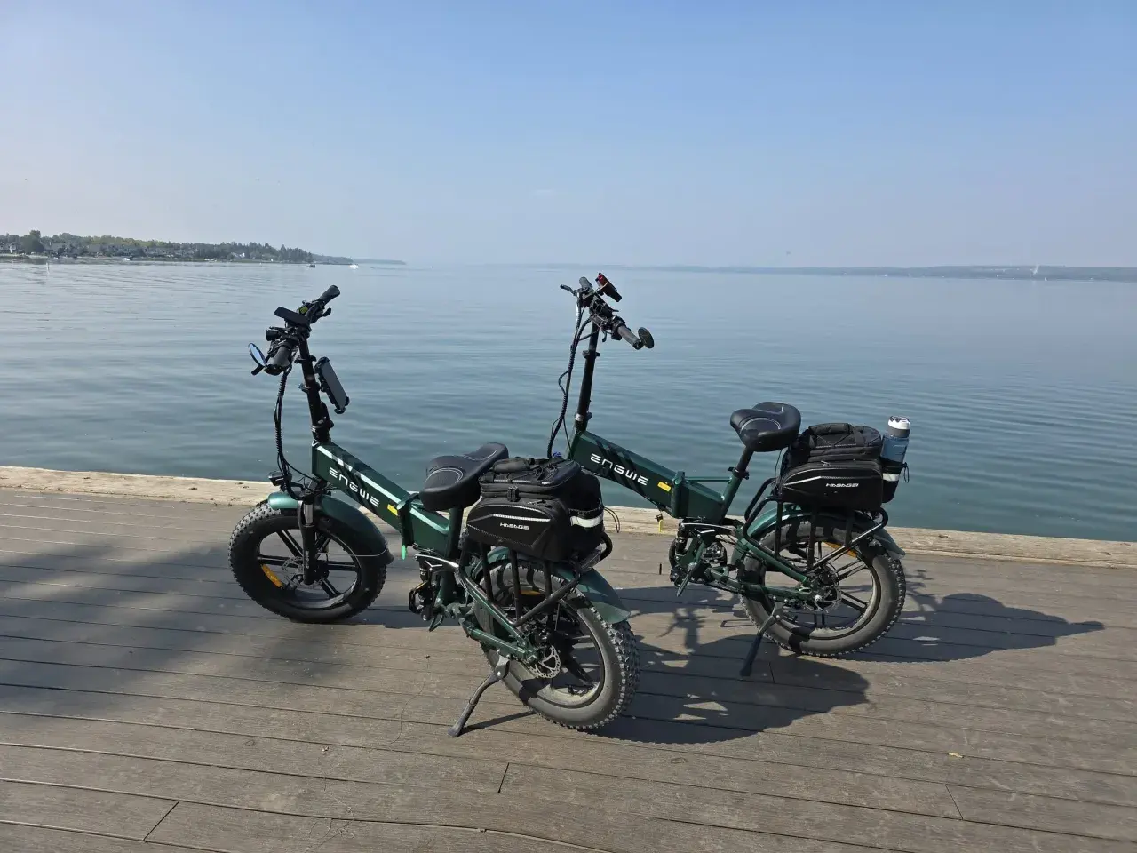 Dwa zielone rowery elektryczne z sakwami, gotowe na wyprawę z zasięgiem 200 km nad spokojną wodą.