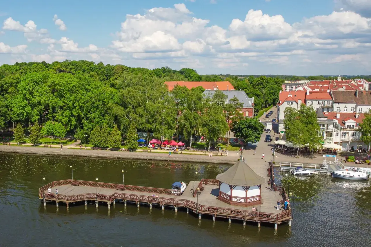 Malownicze mazury miejscowości nad jeziorem, z drewnianym molo, altaną i urokliwą zabudową.