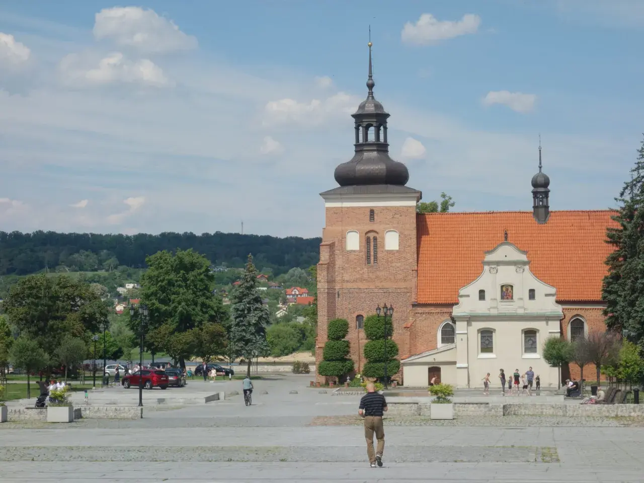 Włocławek atrakcje na weekend: plac z katedrą, zielone drzewa i ludzie spacerujący w słoneczny dzień.