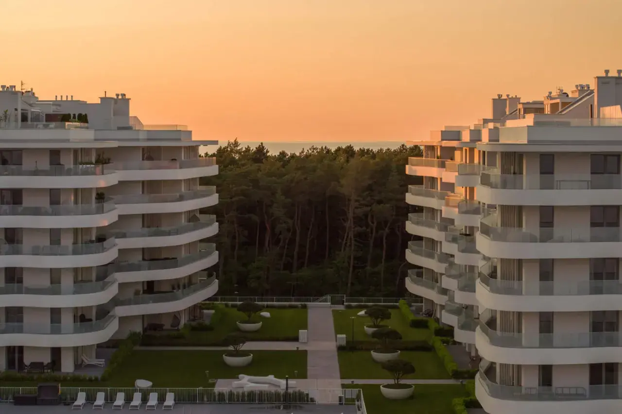Nowoczesne apartamenty w Rogowie z widokiem na las i morze. Zachód słońca maluje niebo na pomarańczowo.