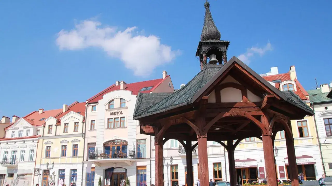 Rzeszów rynek z drewnianą altaną i kamienicami. Słońce świeci, a na niebie widać chmury.
