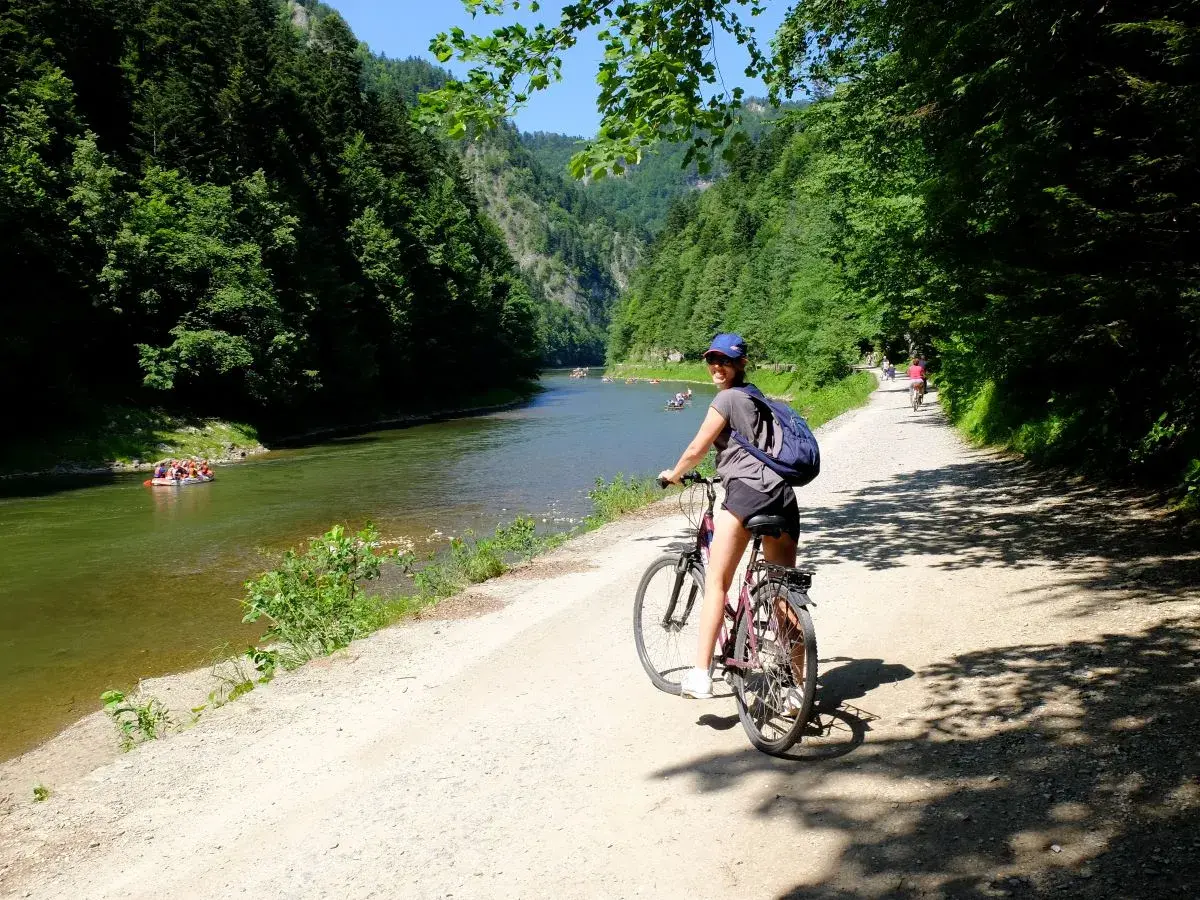 Dziewczyna na rowerze na malowniczej trasie rowerowej w Szczawnicy. W oddali widać tratwy na rzece.