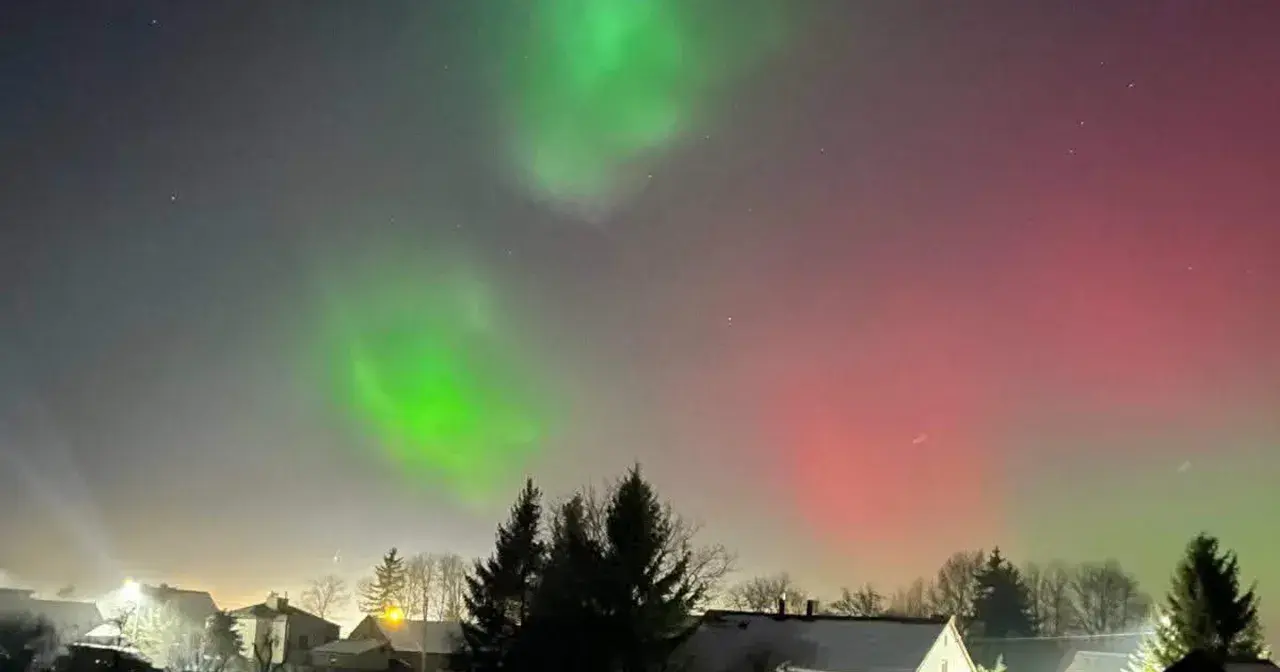 Zielona i czerwona zorza polarna nad domami. Zastanawiasz się, ile trwa zorza polarna? To zjawisko może trwać od kilku minut do kilku godzin.
