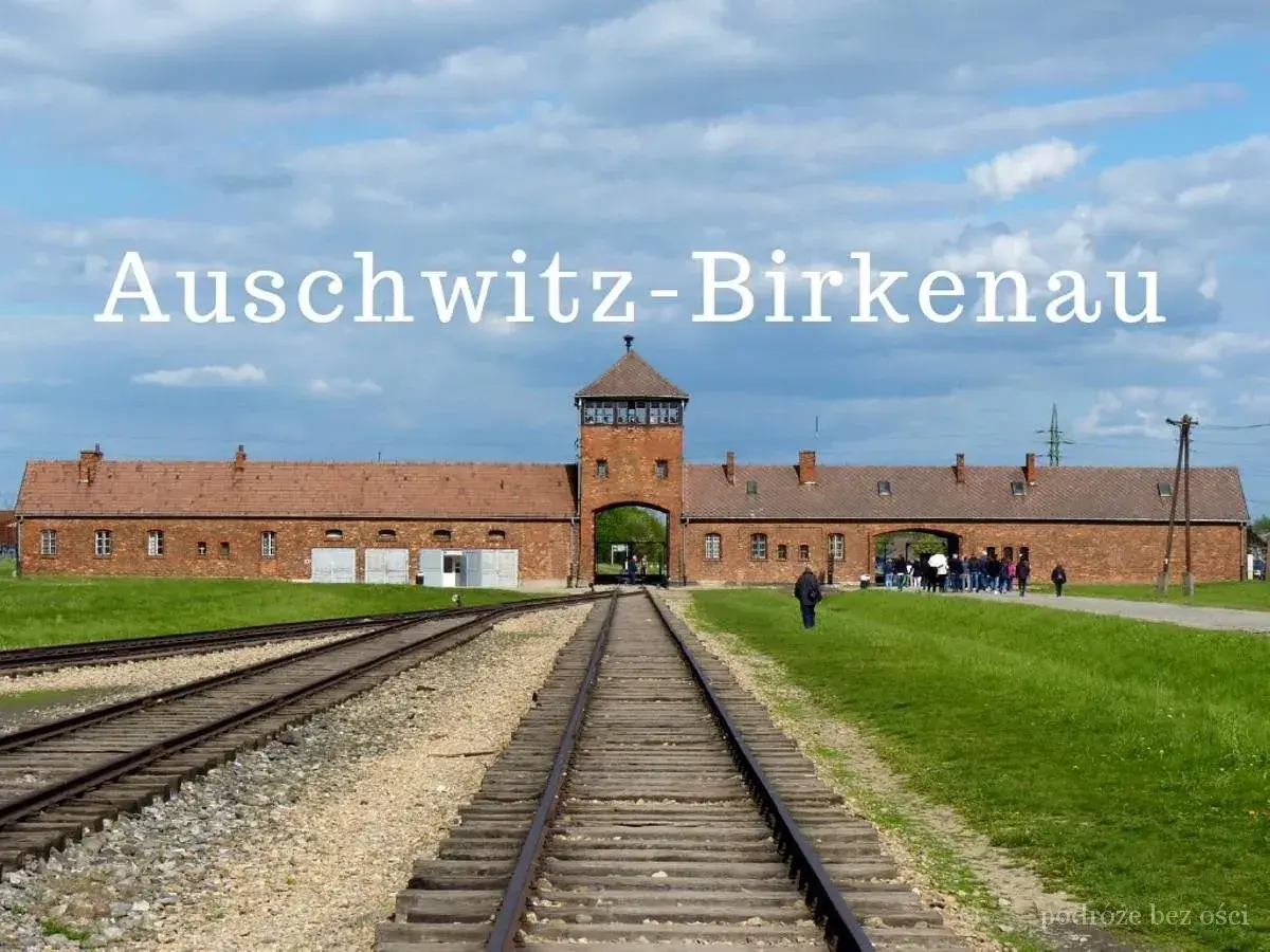 Brama obozowa Auschwitz-Birkenau, gdzie historia przypomina o tragedii. Tłum zwiedzających podąża torami.