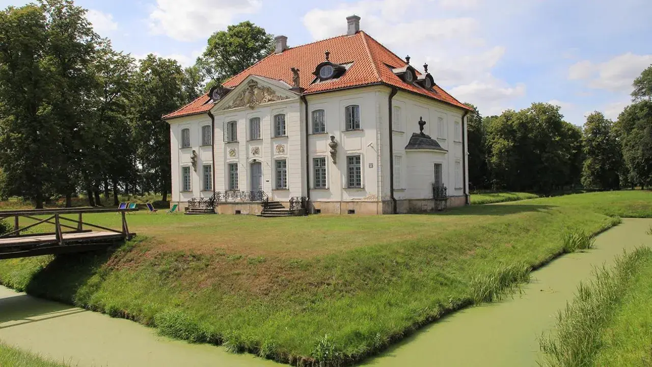 Pałac w Choroszczy otoczony fosą i zielenią. Drewniany mostek prowadzi do rezydencji.