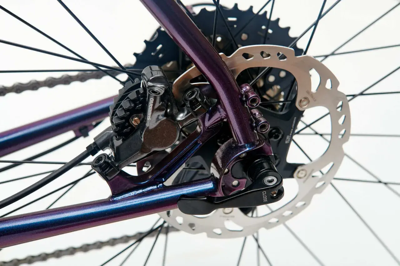 Błyszcząca, fioletowa rama roweru z widoczną sztywną osią, przerzutką Shimano i tarczą hamulcową.