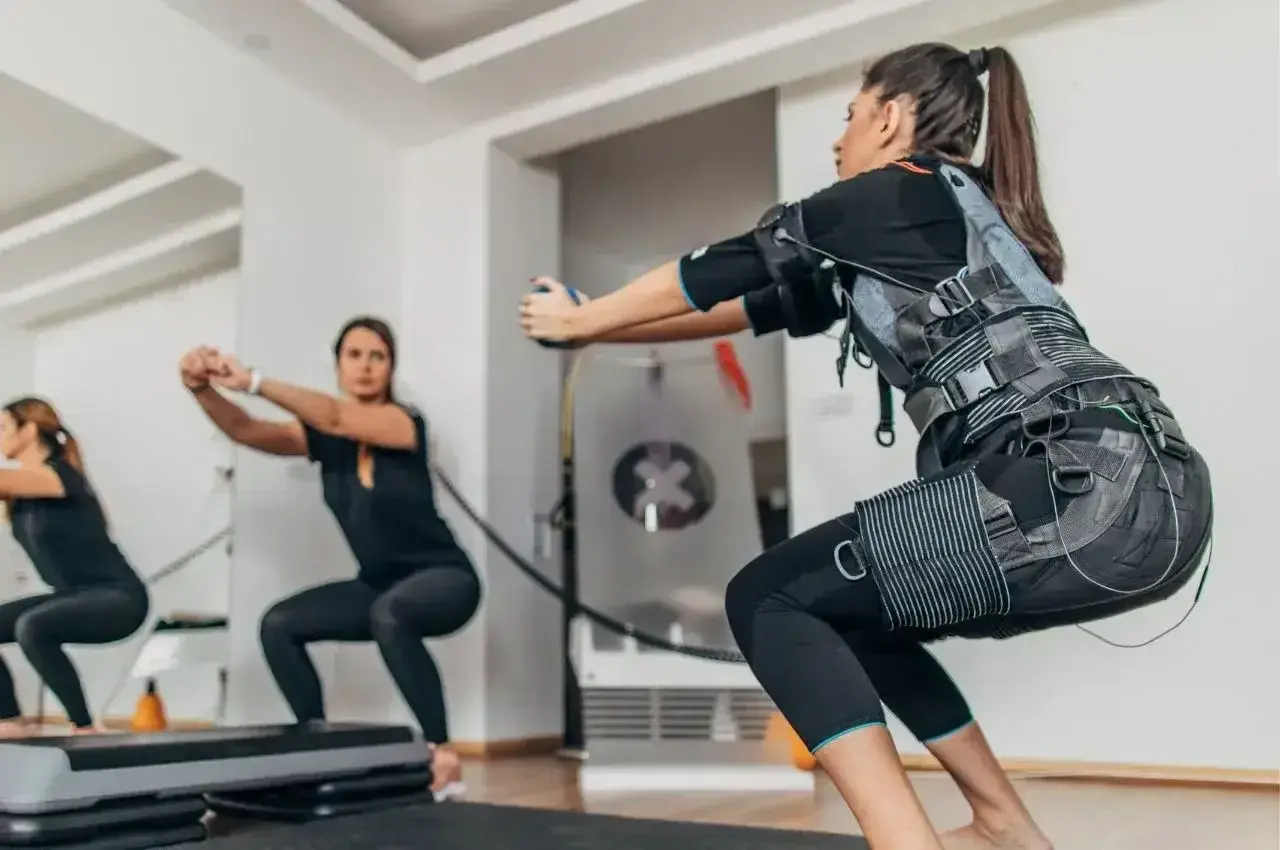 Kobiety w kamizelkach EMS wykonują przysiady. Trening z elektrostymulacją mięśni (EMS) to przyszłość fitnessu.