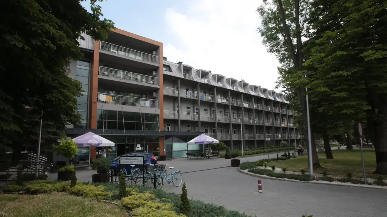 Budynek sanatorium z balkonami i drzewami. Miejsce idealne do wypoczynku i regeneracji, gdzie balneologia odgrywa kluczową rolę.