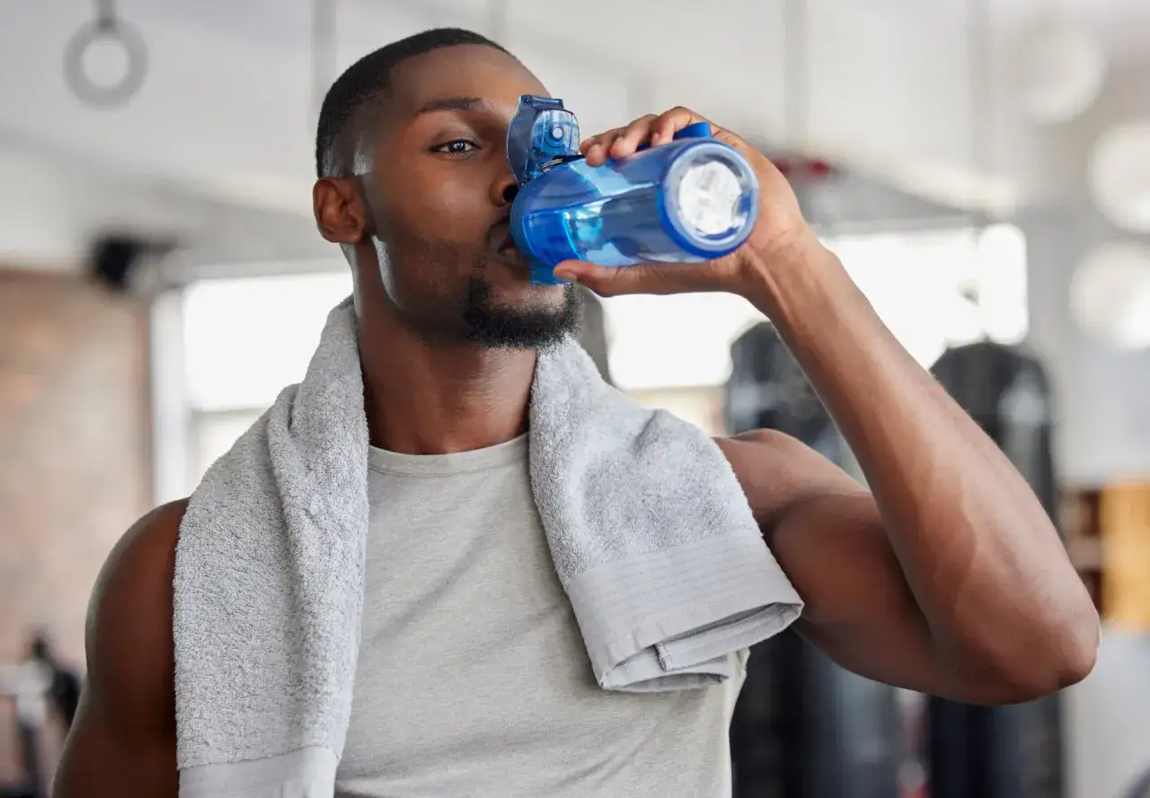 Mężczyzna po treningu pije wodę z niebieskiej butelki. To idealny moment, kiedy pić elektrolity, by uzupełnić płyny.