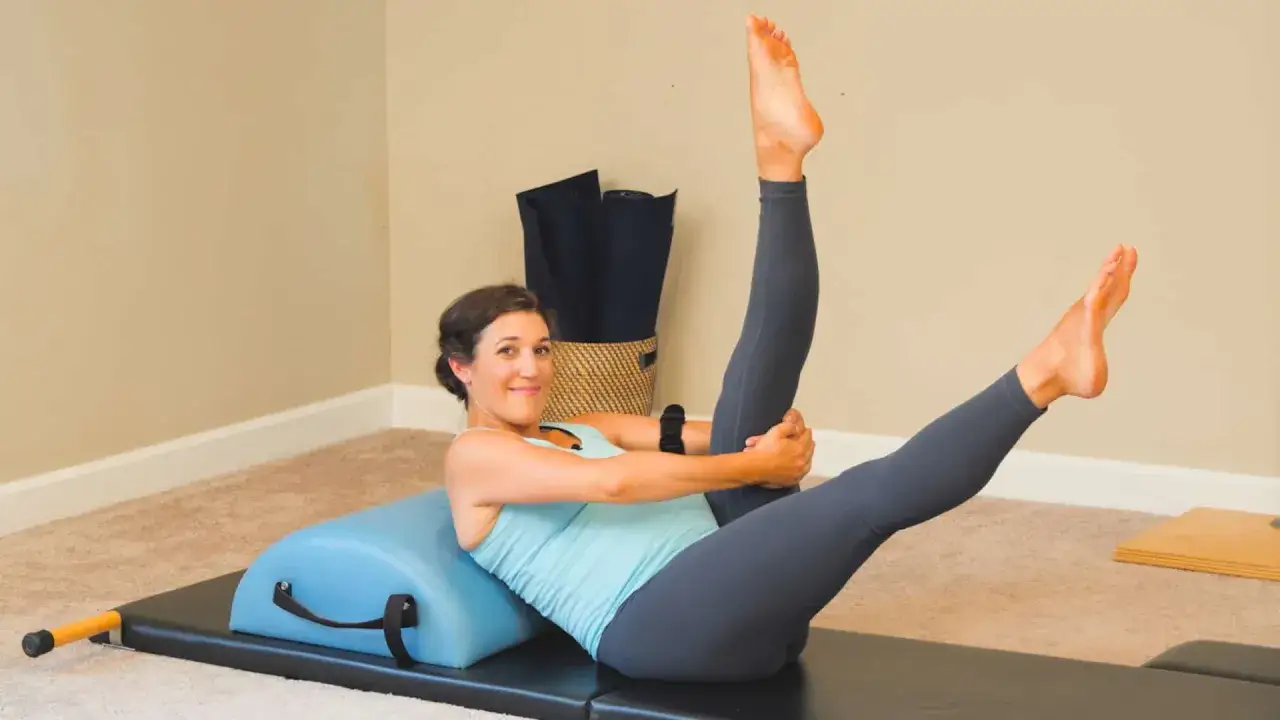 Kobieta ćwiczy pilates w ciąży, leżąc na macie z wałkiem.