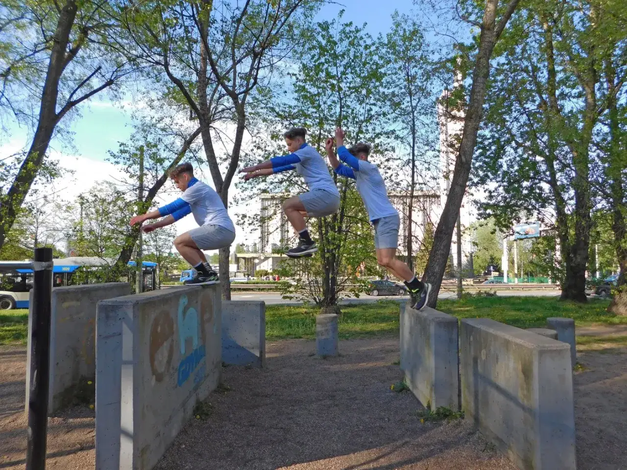Trzech młodych mężczyzn skacze przez betonowe przeszkody, pokazując, parkour co to jest: dynamiczne pokonywanie terenu.