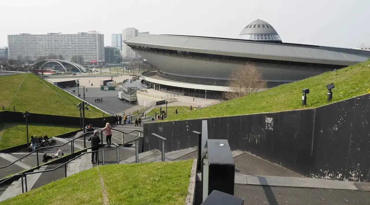 Nowoczesna architektura Spodka i MCK w Katowicach, województwo śląskie, z zielonymi skarpami i ludźmi spacerującymi po schodach.